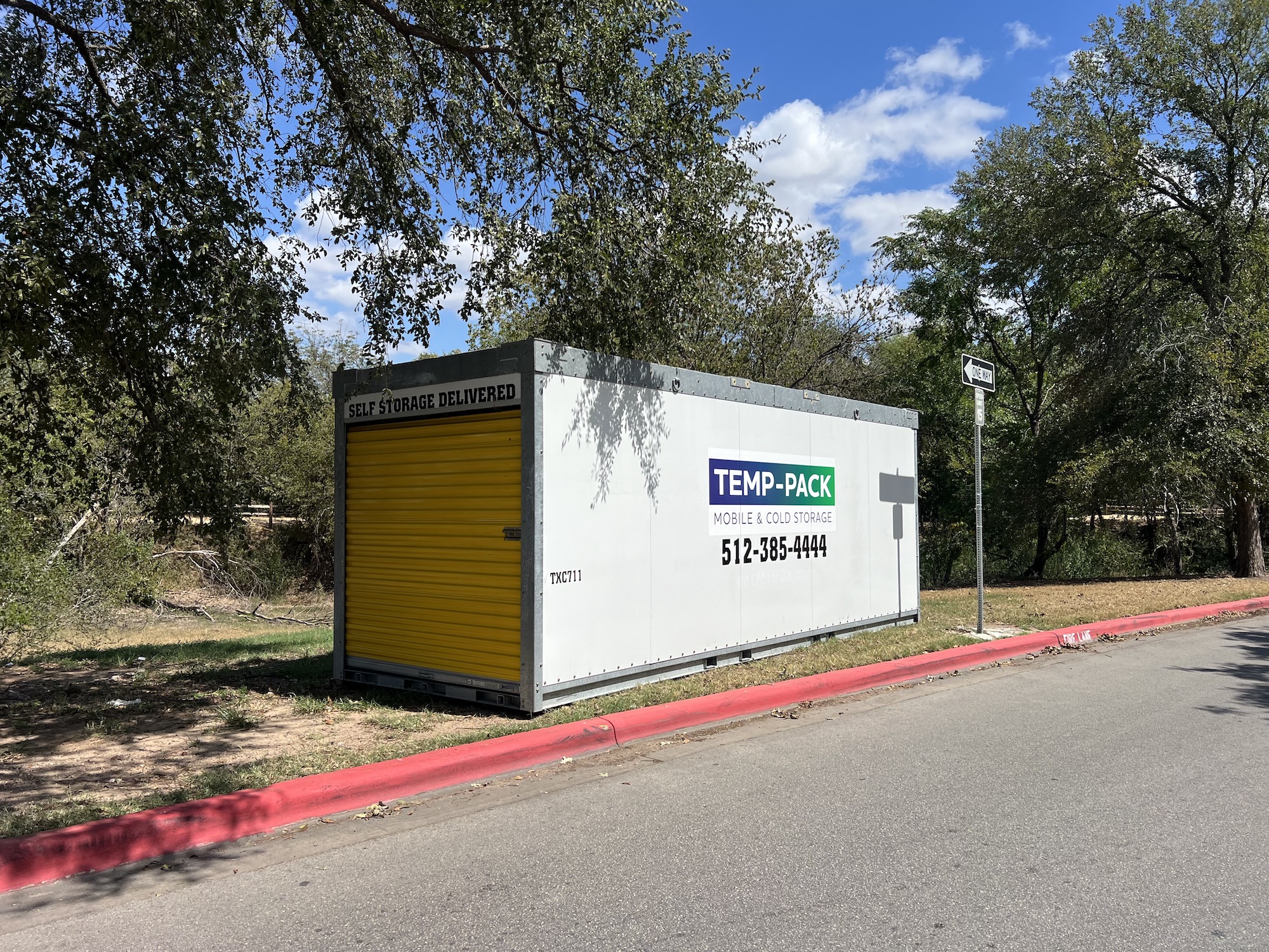 TEMP-PACK container beside trees and a paved access lane